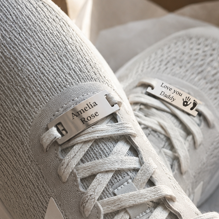 Pair of light gray sneakers with personalised shoe tag charm on a soft beige background