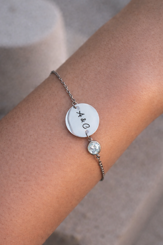 Silver bracelet with a round charm and diamond on a wrist against a neutral background