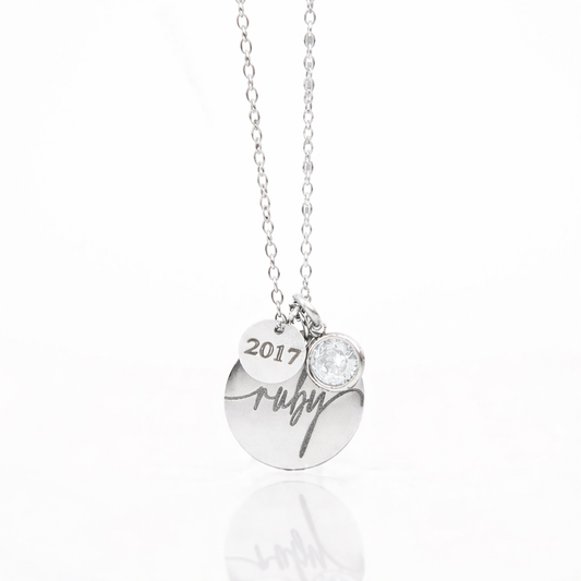 Silver necklace with a heart-shaped pendant, '2017', and 'Ruby' engraved on a white background. With the April birthstone