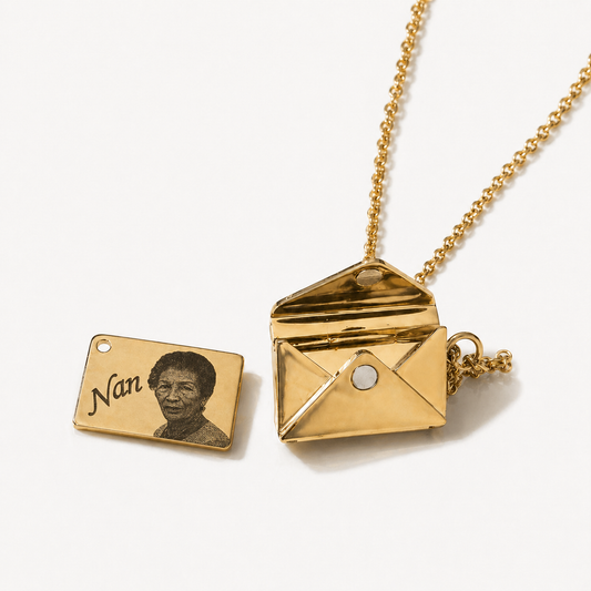 Gold necklace with an envelope pendant and a rectangular tag featuring a engraving of a person.
