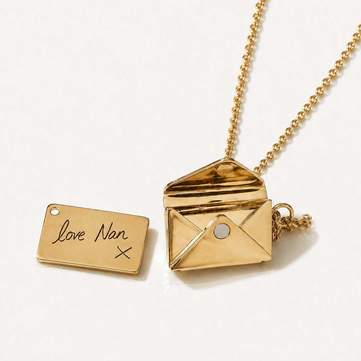 Gold necklace with an open envelope pendant and a rectangular tag on a white background
