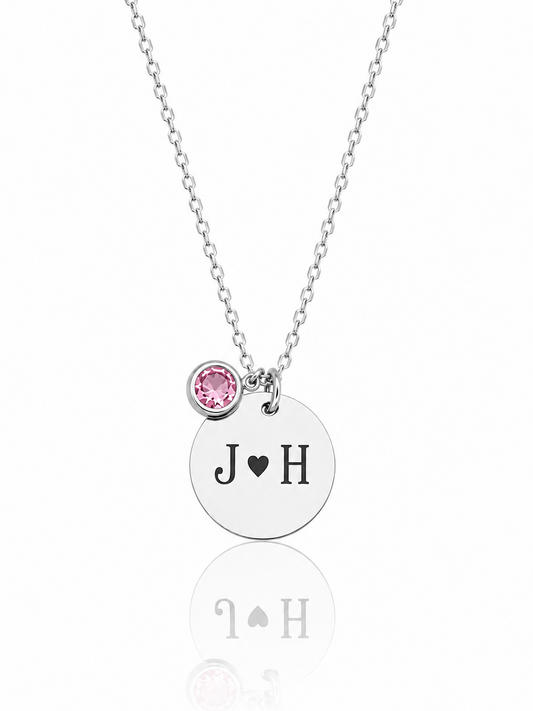 Necklace with a round pendant featuring initials 'J' and 'H', and a pink gemstone on a white background.