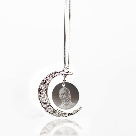 Silver crescent moon car charm with engraved face on a white background