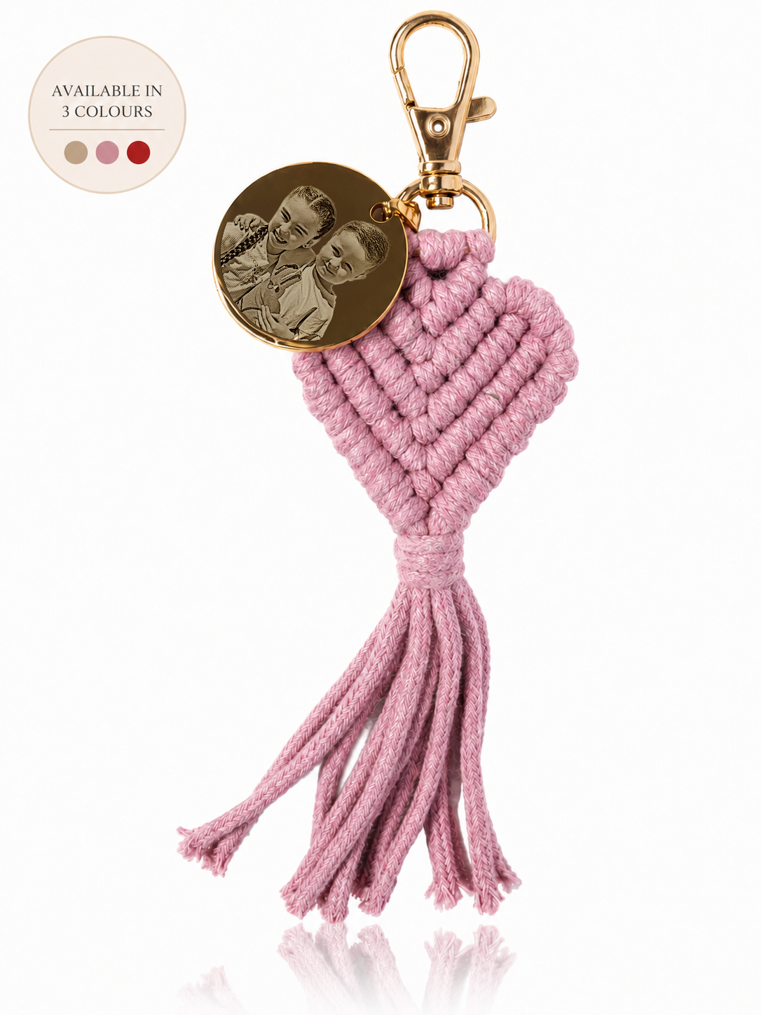 A pink knotted cord heart keychain with a gold-tone clasp, a round engraved metal charm, and a tassel, shown on a white background with a small circular inset indicating available colors.