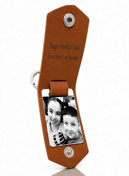 A brown leather birthday gift keychain for Dad, featuring a photo slot with a black-and-white photo of two children and engraved text reading 'Happy Birthday Dad Love Ruby &ayne'.