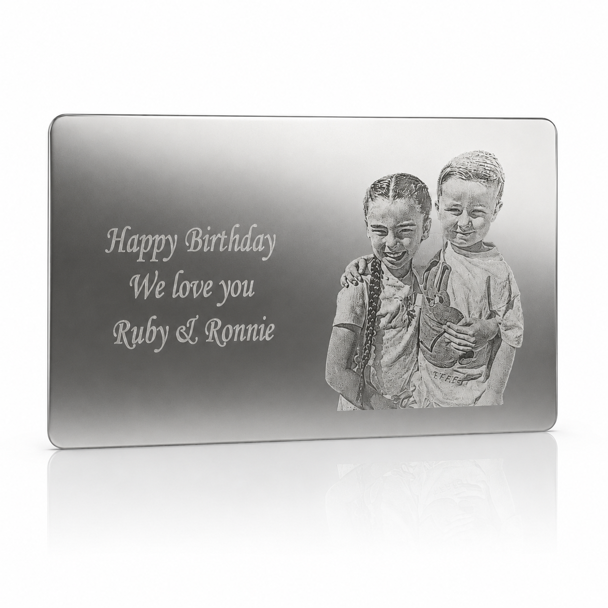 A rectangular silver-toned plaque or engraved gift board shown on a clean white background. The front features the engraved text 'Happy Birthday We love you Ruby & Ronnie' alongside a grayscale portrait of two children holding a teddy bear.
