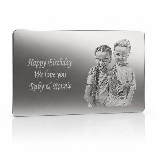 A rectangular silver-toned plaque or engraved gift board shown on a clean white background. The front features the engraved text 'Happy Birthday We love you Ruby & Ronnie' alongside a grayscale portrait of two children holding a teddy bear.