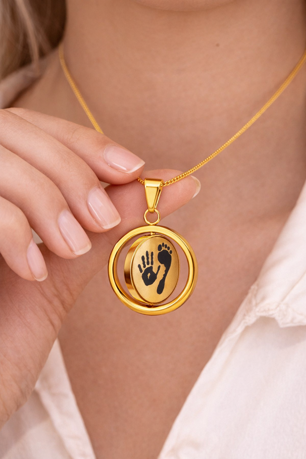 Gold necklace with a pendant featuring a hand and foot print held by a person.