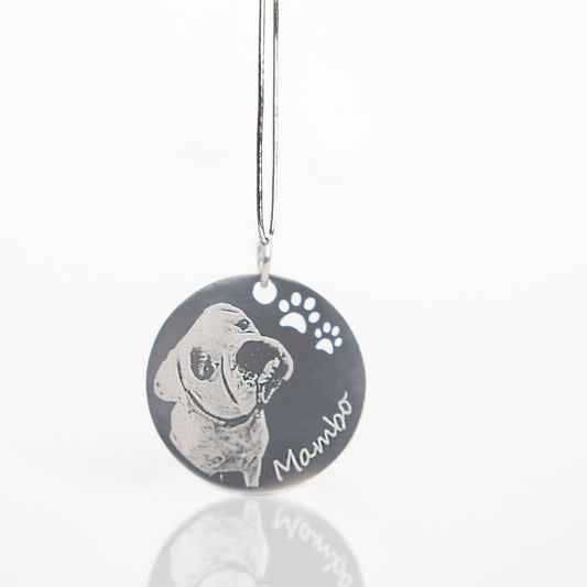 A round black pet memorial pendant with a silver metal wire hanger, featuring a custom engraved dog portrait, paw prints, and the name 'Mambo'.